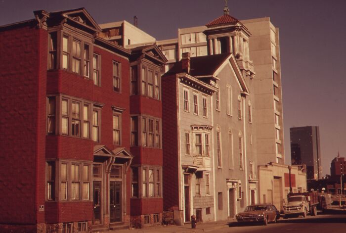 Vintage cityscape from 1973 featuring classic brick buildings and parked cars on a sunny street.