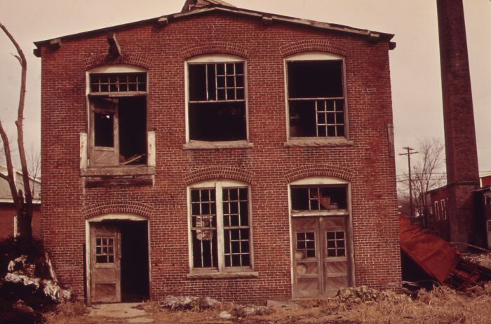 Old brick building from 1973 with broken windows, showcasing decay and industrial architecture.