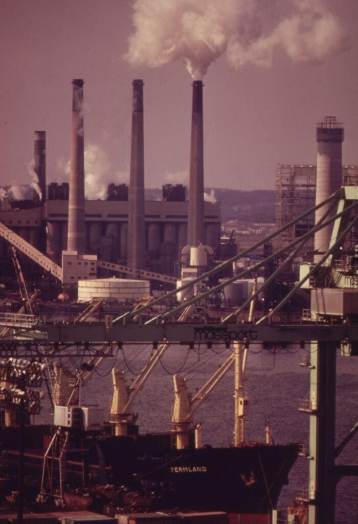Industrial scene from 1973, showing a busy port with cranes and smokestacks releasing smoke into the sky.