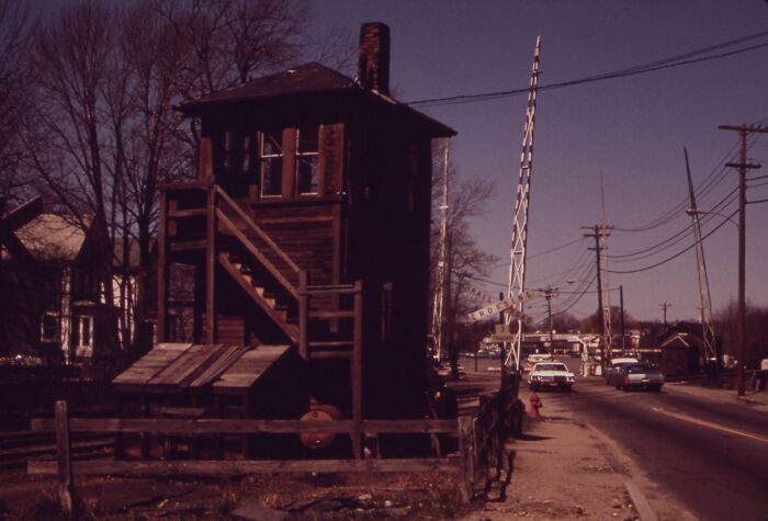 Historic railroad crossing and signal tower in a small town, 1973, showcasing vintage architecture and transportation.