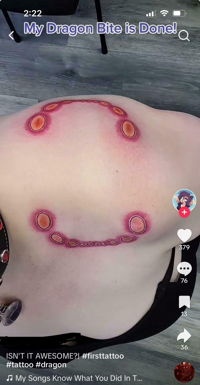 Tattoo with a circular design resembling dragon bite marks, featuring red and orange highlights on a person's back.