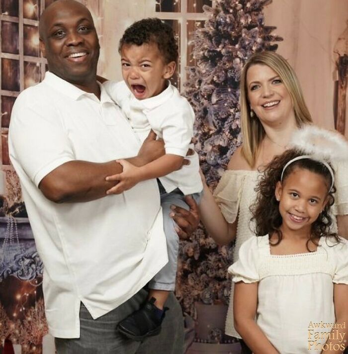 Awkward family photo with smiling parents, crying toddler, and smiling girl in matching white outfits.