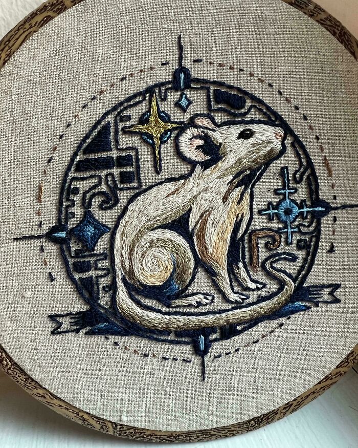 Embroidered design of a detailed mouse with geometric and star patterns in blue and gold tones on fabric.