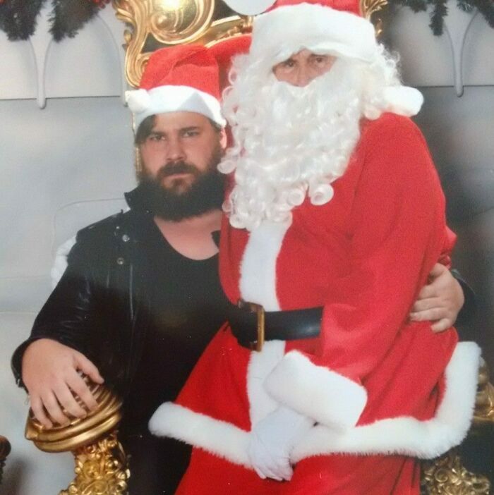 Man in a Santa hat sits awkwardly next to a Creepy-Santas figure on a golden throne.
