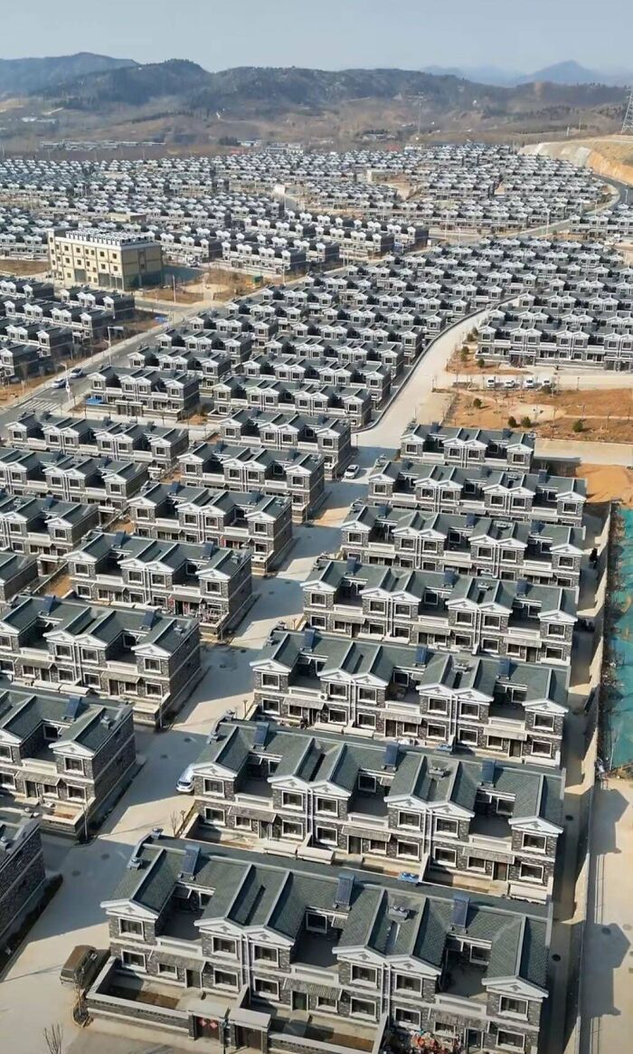 Dense housing in an urban area, showcasing repetitive rows of identical houses under clear skies.