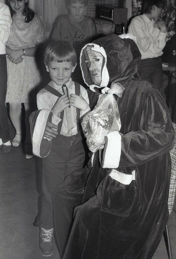 Child standing beside a creepy Santa in a dimly lit room.