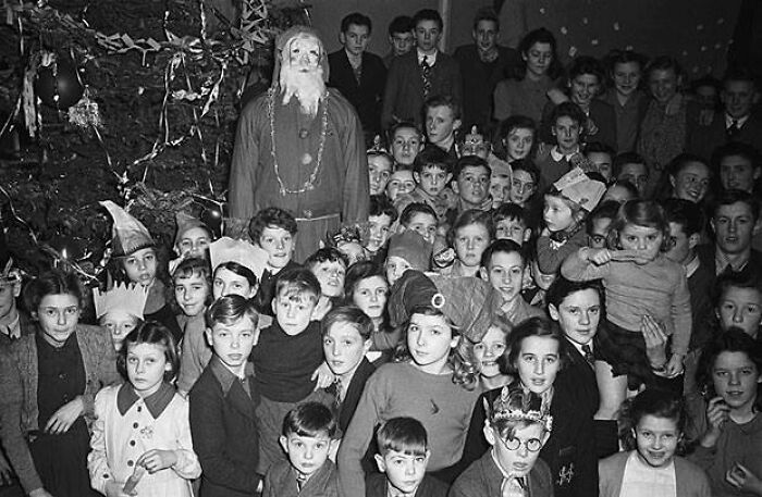 Group of children gathered around a creepy Santa figure, posing for a vintage holiday photo.