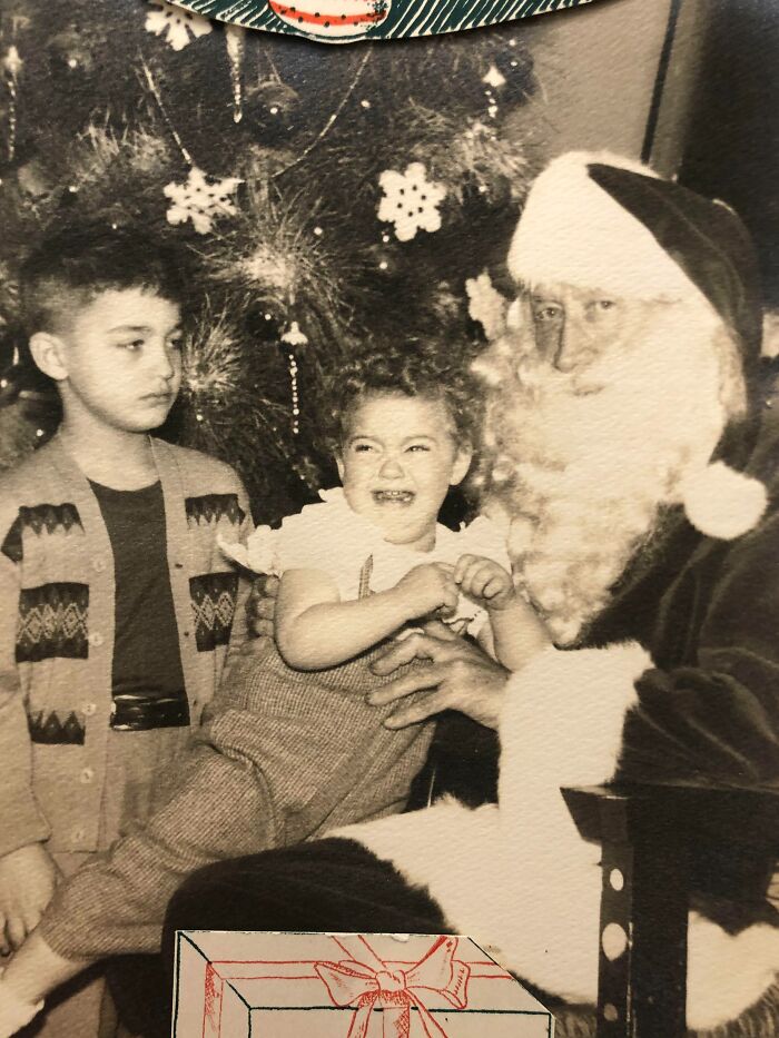 Vintage photo of a child crying on Santa's lap, capturing the eerie charm of Creepy-Santas with a festive Christmas tree behind.