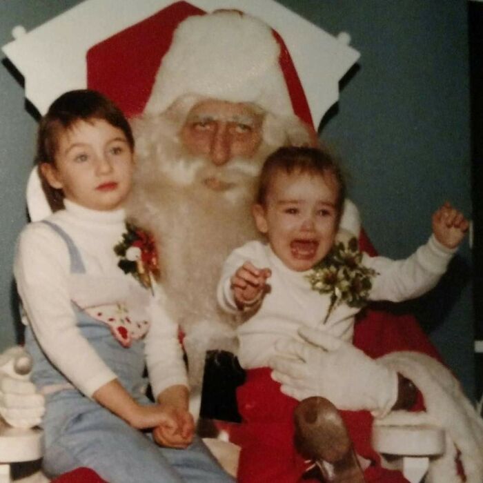 Two children sitting with a creepy Santa, one looking uneasy and the other crying.