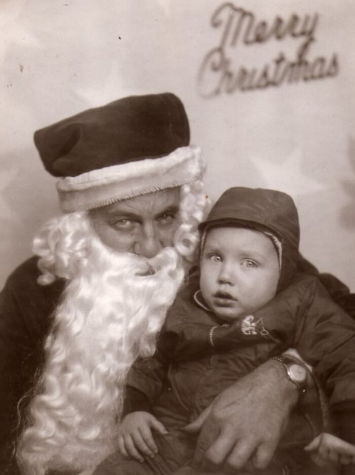 Creepy Santa with a child in an old black-and-white photo under a "Merry Christmas" sign.