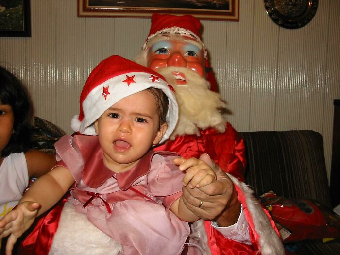 Creepy-Santas: Child looks uneasy sitting with a Santa wearing a mask.