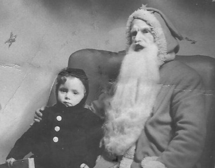 Vintage photo of a child sitting next to a Santa with an eerie expression, capturing a classic Creepy-Santas moment.