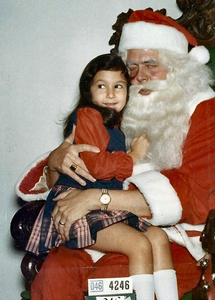 A child sitting on a creepy Santa's lap, wearing a plaid dress, with a cautious expression.