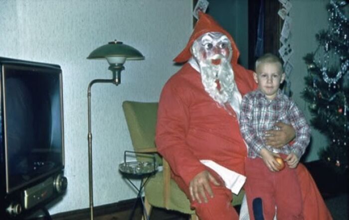 Creepy Santa in red suit with a child on his lap next to a vintage TV and Christmas tree.