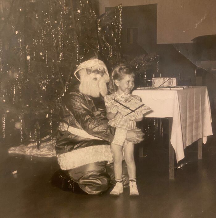 Vintage photo of a child smiling next to a Creepy-Santa by a Christmas tree.