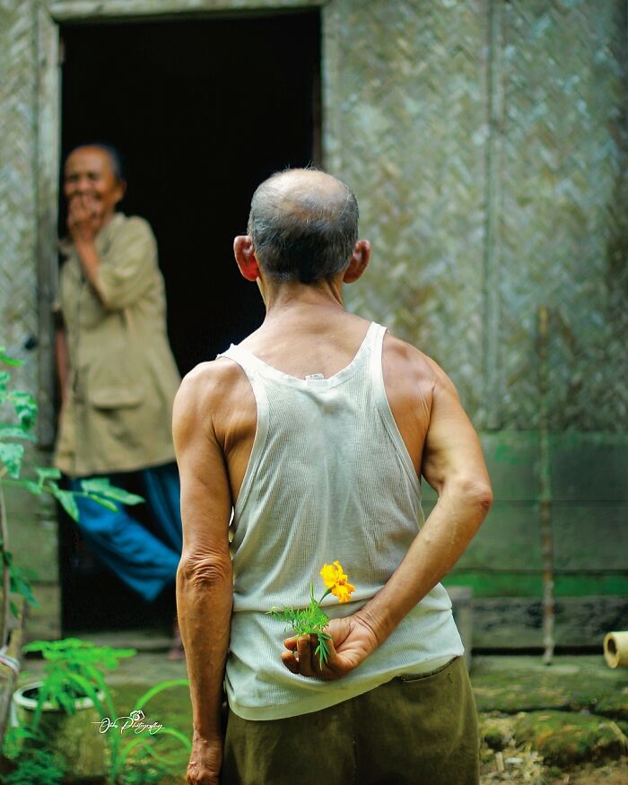 Indonesian photographer captures simple life moment of a man hiding a flower behind his back, facing a smiling woman.
