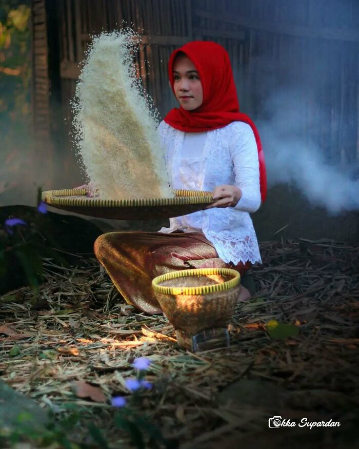 Indonesian woman in traditional attire sifting rice outdoors, capturing simple life moments.