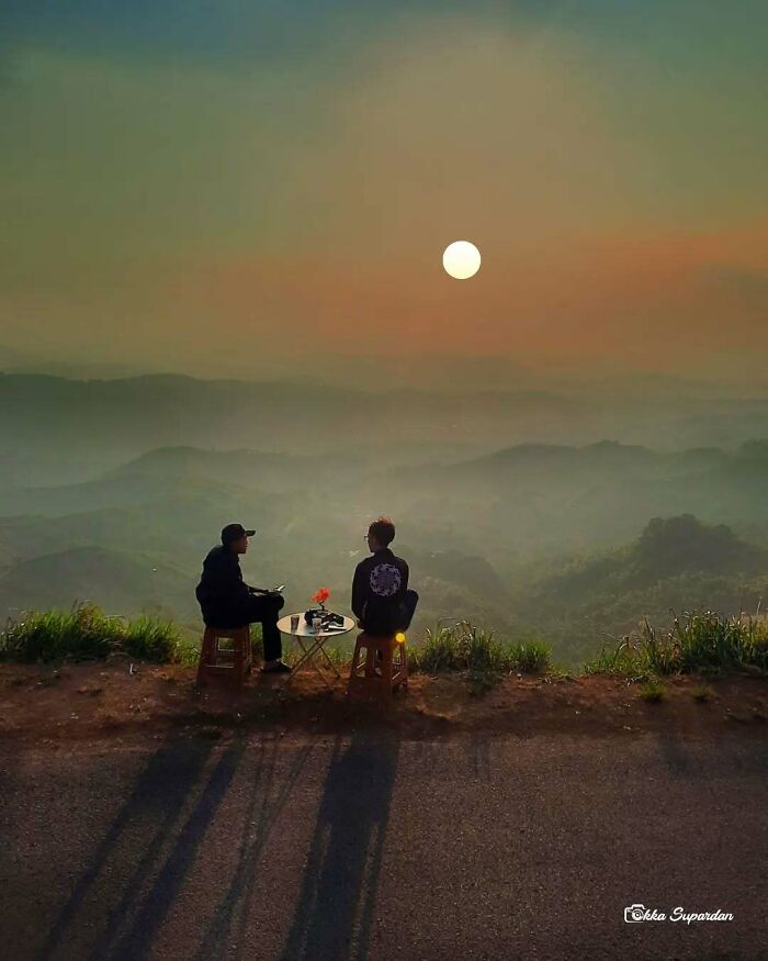 Two people enjoying a simple life moment, sitting outdoors at sunset with a scenic view in Indonesia.