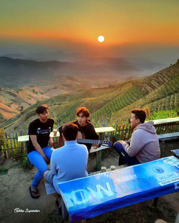 Indonesian photographer captures friends sitting at a hillside bench, watching sunset, emphasizing simple life moments.