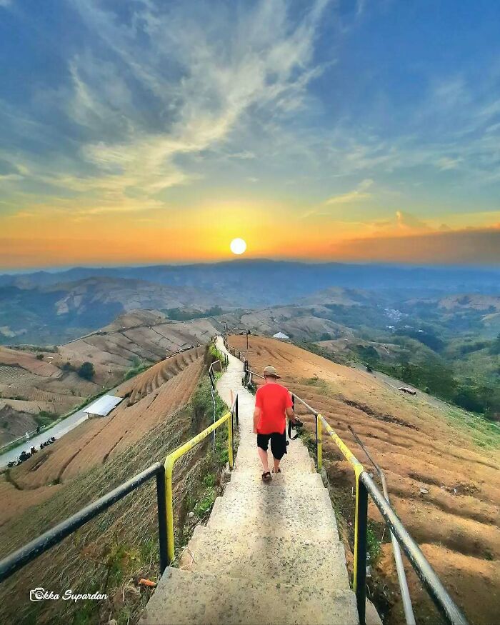 Indonesian photographer captures a stunning sunset over terraced hills as a person walks down a path.