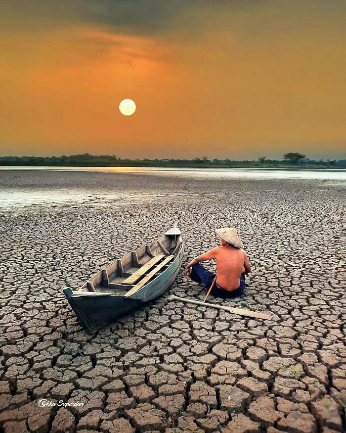 Indonesian photographer captures a serene moment of a man beside a boat on c*****d earth under a setting sun.