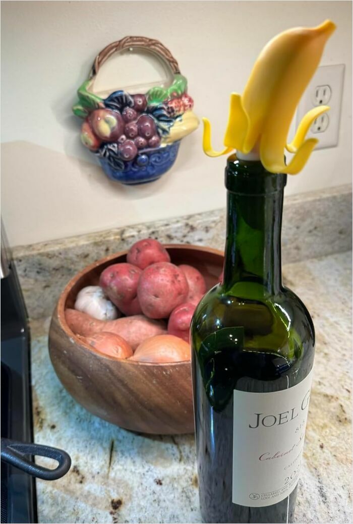Wine bottle with a banana-shaped stopper, surrounded by a rustic kitchen setting with a fruit-themed wall decor.