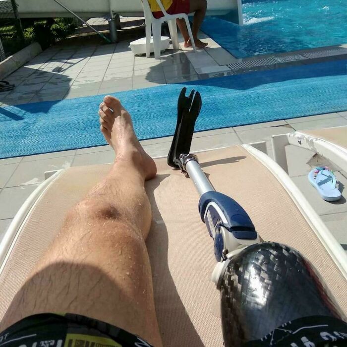 Man lounging by a pool with a prosthetic leg, enjoying a sunny day. Nothing interesting happening around.