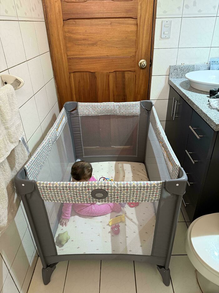 Baby in a playpen in bathroom, showcasing a dad's creative childcare solution.