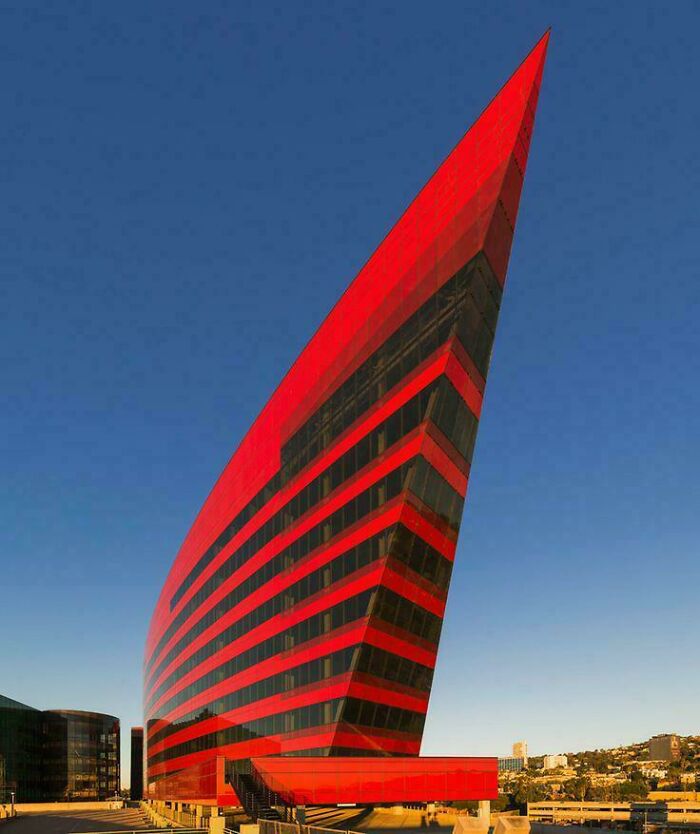 Angular red and black building with an imposing shape, exuding a supervillain headquarters evil aura under clear blue sky.