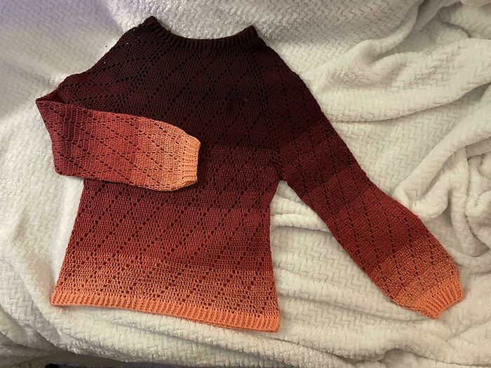 Crochet enthusiasts showcasing a handmade gradient sweater with intricate stitch patterns laid on a soft blanket.