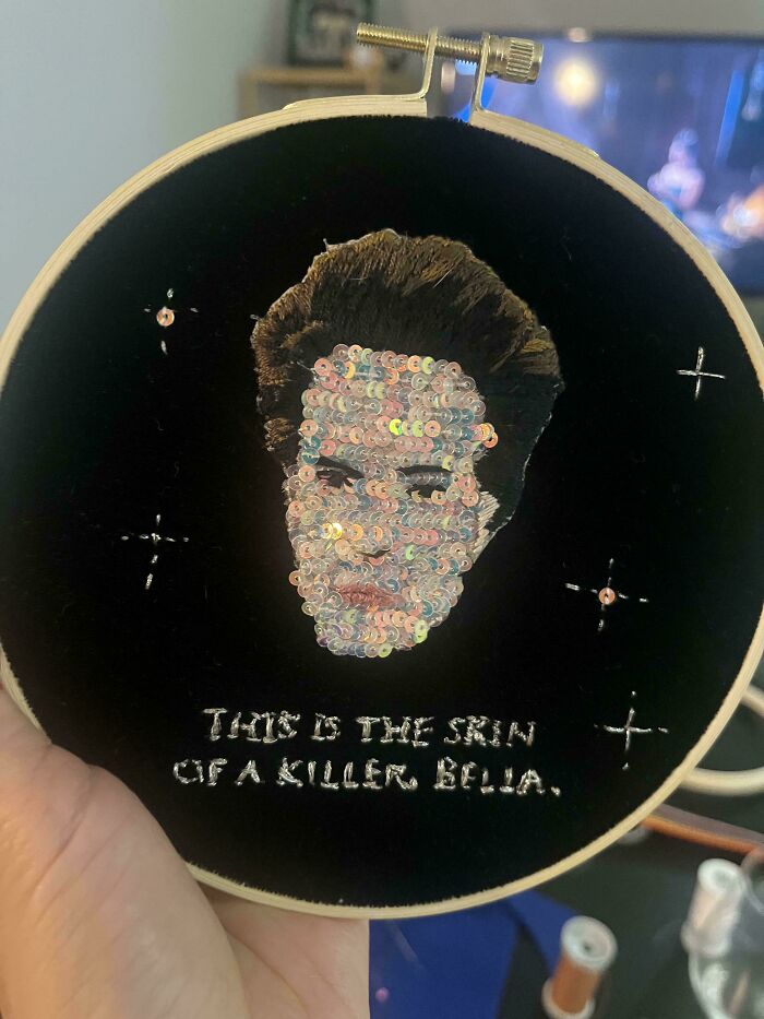 Handcrafted embroidery design with sequins on black fabric depicting a detailed face and silver stitched text.