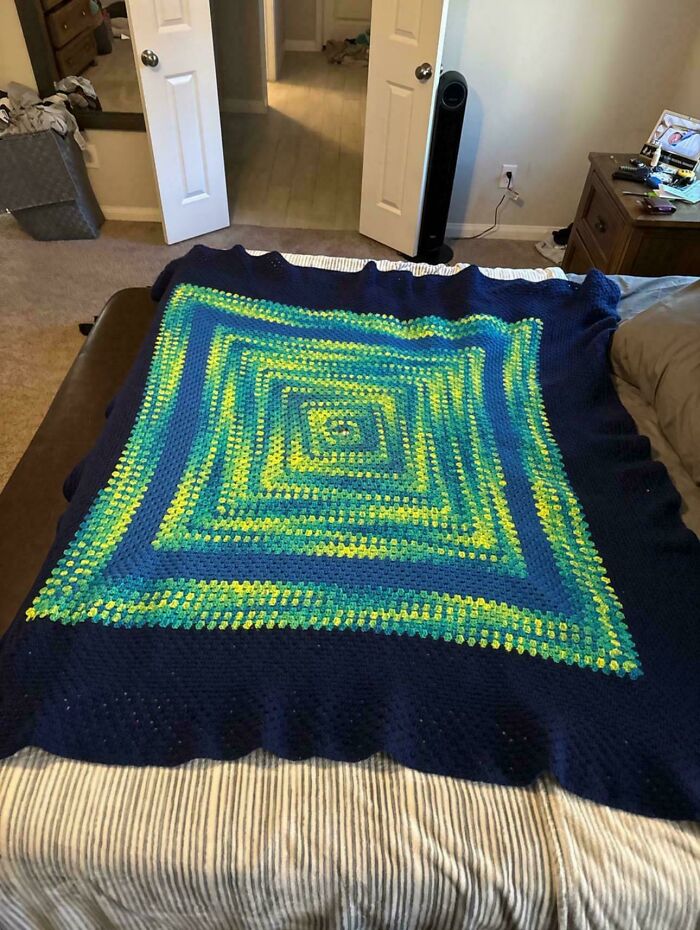 Colorful crochet blanket with blue, green, and yellow squares displayed on a bed by a proud crochet enthusiast.