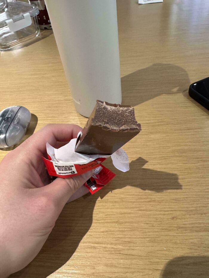 Partially unwrapped chocolate bar with a bite taken sideways, illustrating one job fail on a wooden table surface.