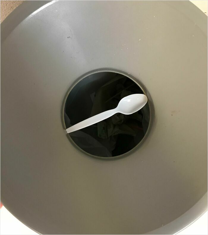 Plastic spoon perfectly fitting in a circular trash can opening, illustrating a satisfying-perfect-fit moment.