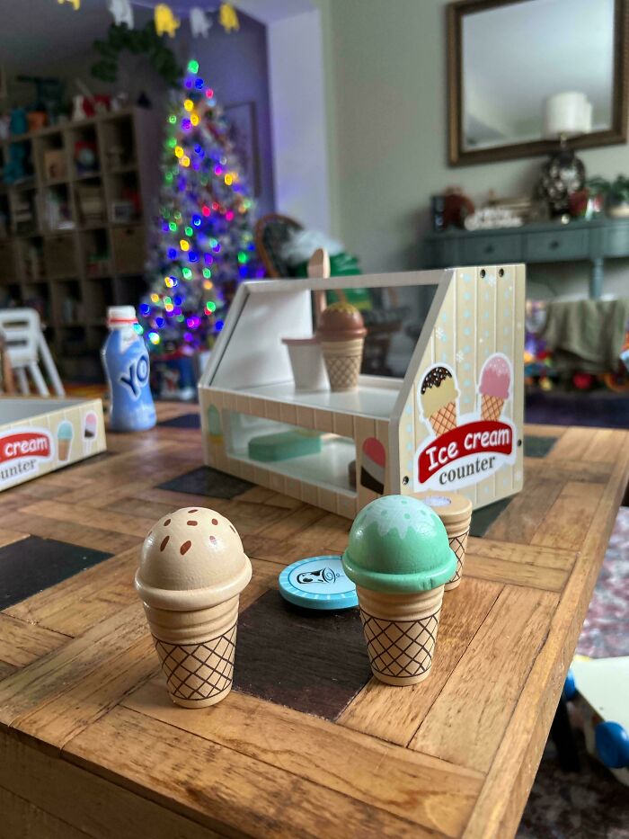 Toy ice cream set on a table with a decorated Christmas tree in the background; showcasing rewarding dad moments.