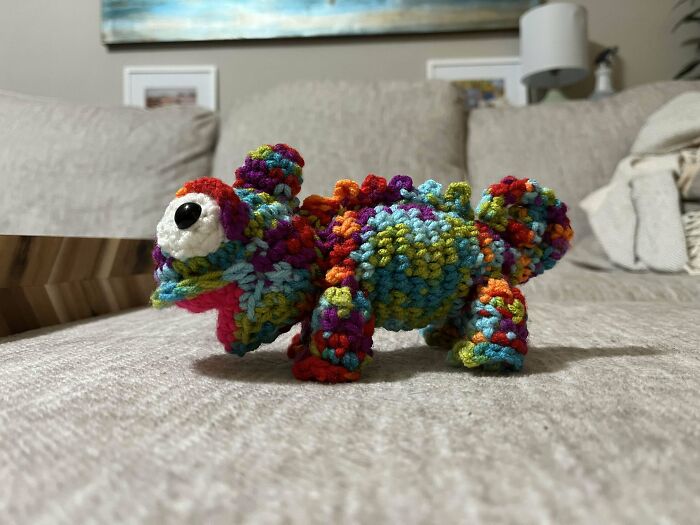 Colorful crochet dinosaur amigurumi crafted by a crochet enthusiast, proudly displayed on a couch in a cozy room.