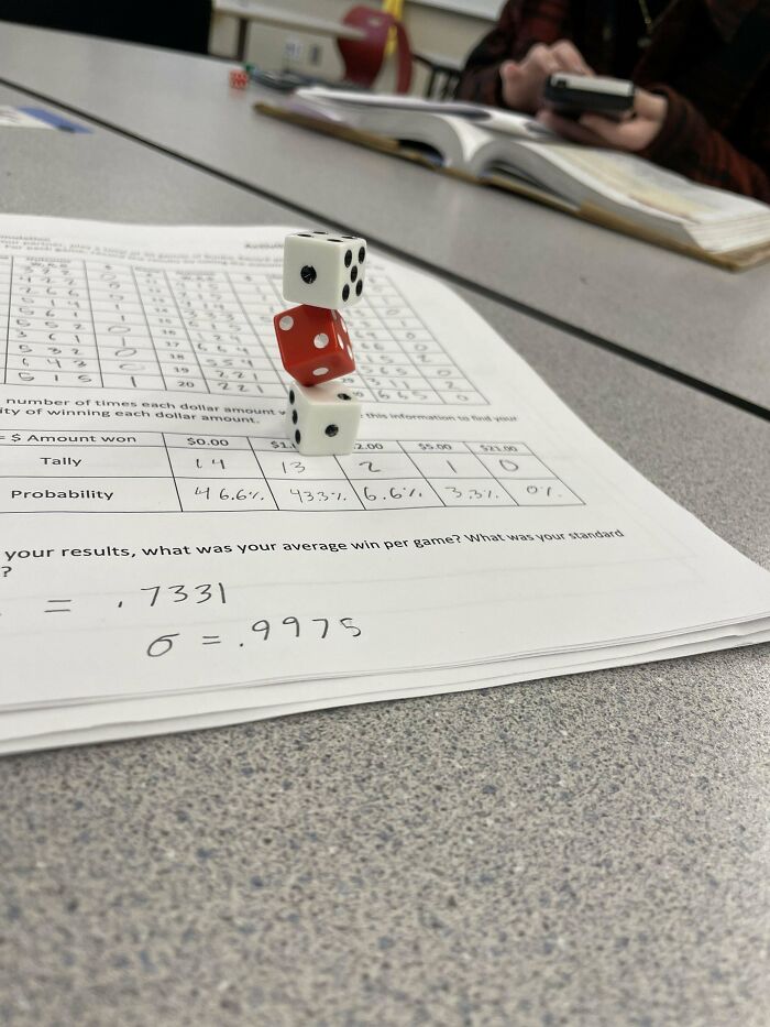 Stacked dice on a math worksheet in a classroom with students in the background, illustrating mundane and uninteresting objects.