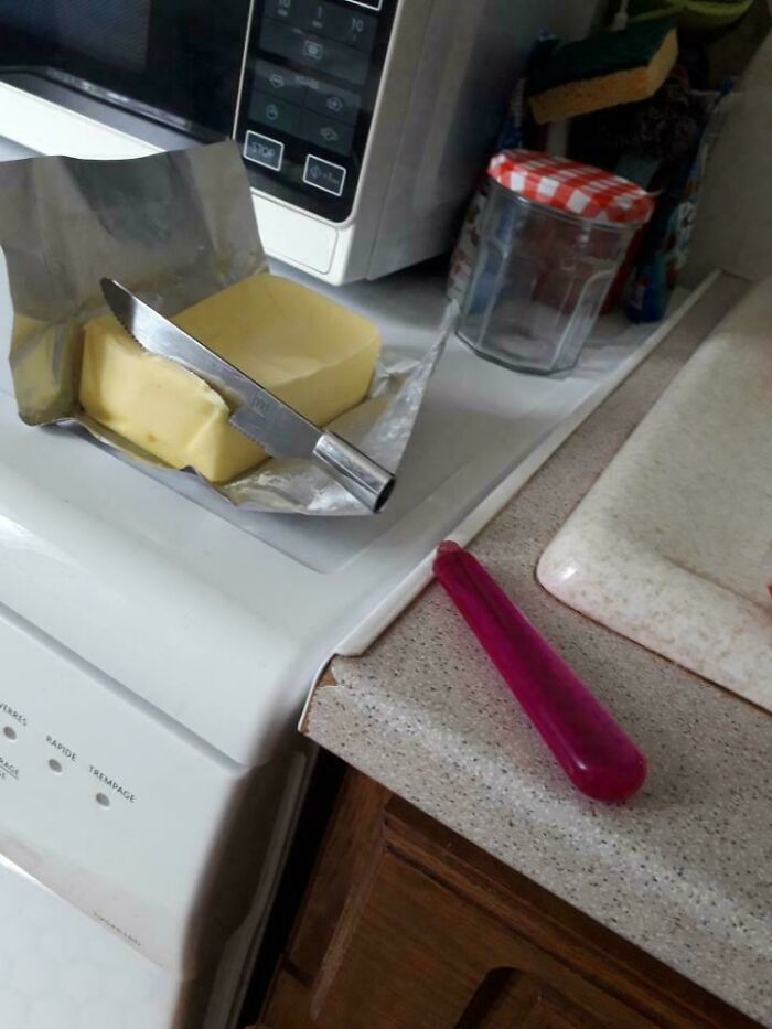 Unremarkable kitchen scene with a butter knife on a block of butter near a microwave and an empty jar.