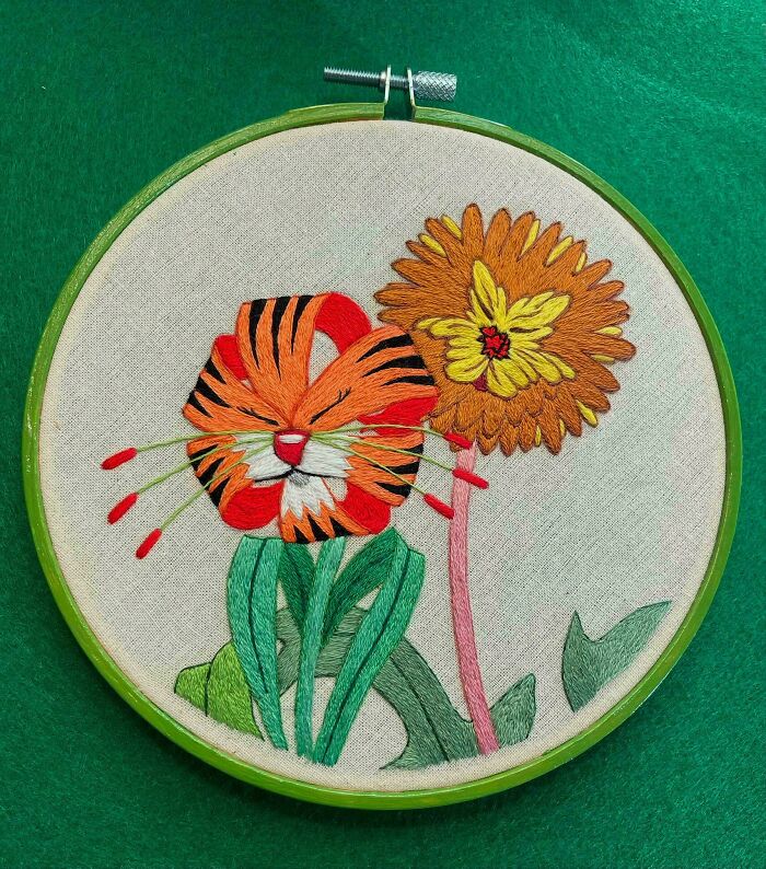 Embroidery designs of a colorful tiger face and vibrant flowers stitched on fabric in a green hoop.