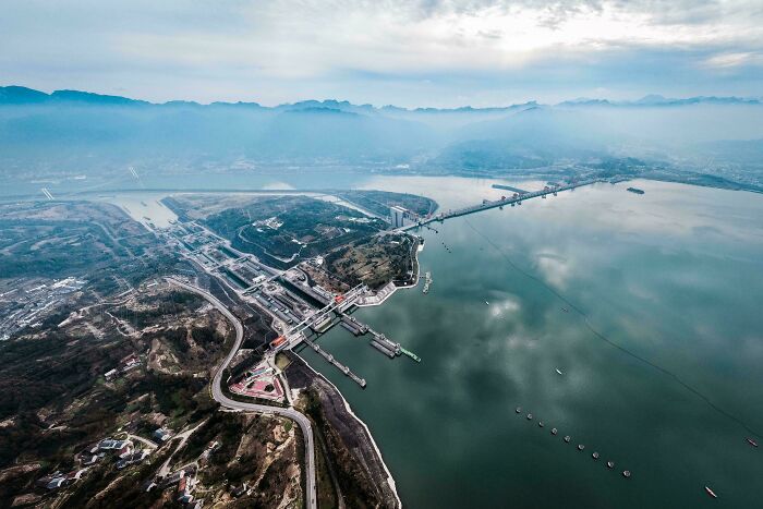 Aerial view of brilliant infrastructure featuring a large dam and bridge over a wide river surrounded by mountains.
