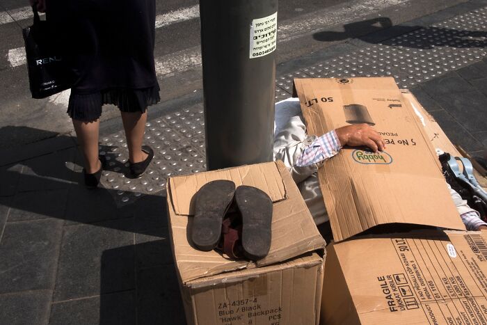 Street scene in Israel showing a person sleeping under cardboard next to a pedestrian in heels.