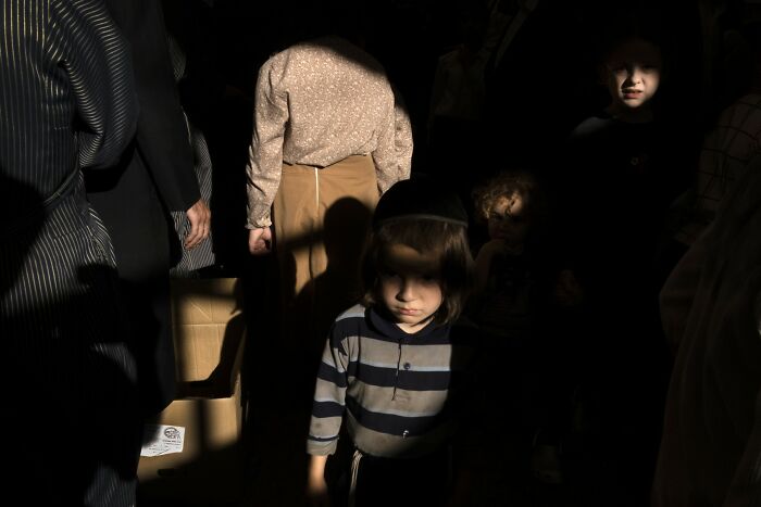 A child in striped clothing stands in a shadowy street scene in Israel, captured by Ilan Ben Yehuda.
