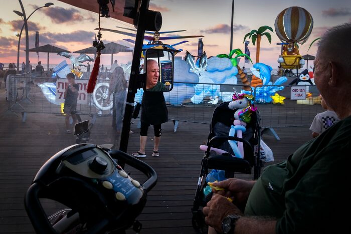Street scene in Israel with people and colorful floats, featuring carnival and transportation elements at sunset.