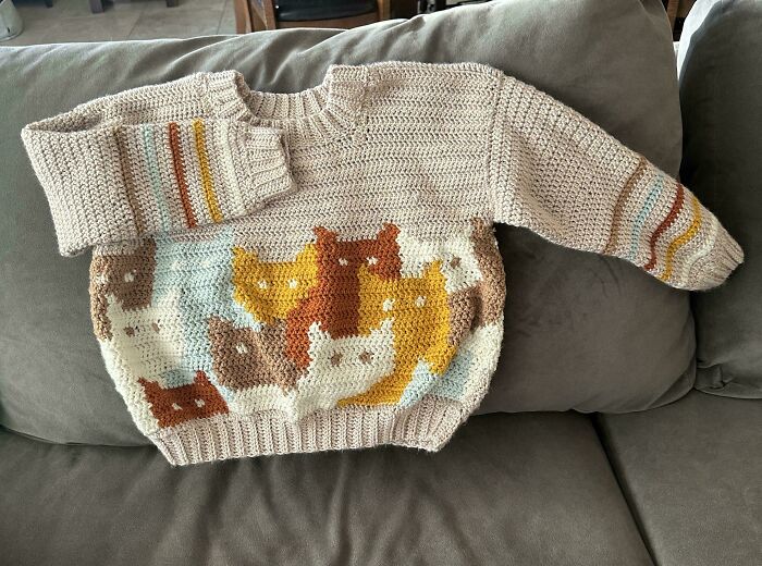 Crochet sweater featuring colorful cat patterns, showcasing a proud crochet enthusiast's creative project on a couch.