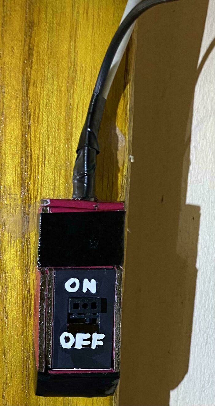 Homemade tech support switch with on and off labels taped to a wooden surface, showing a DIY electrical setup.