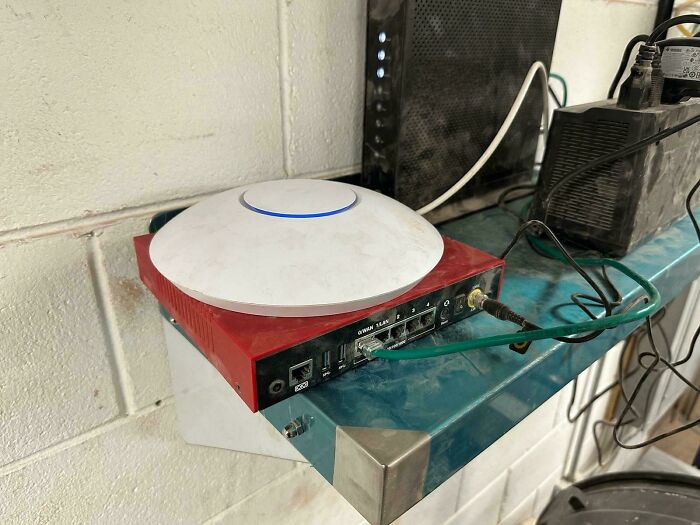 Network router and access point setup with various cables on a metal shelf, showing tech support equipment in use.