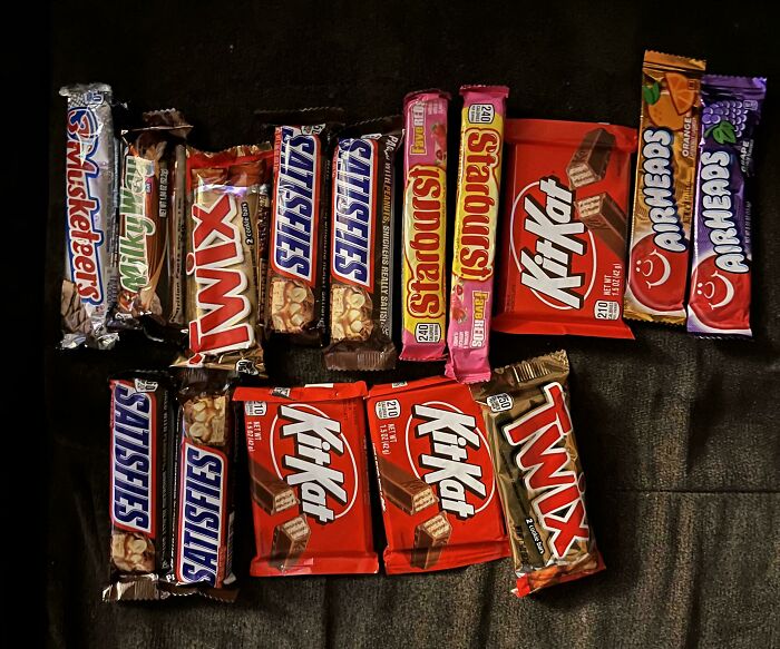 Variety of candy bars, including Snickers and Kit Kat, arranged on a dark surface. Mildly interesting assortment for amusement.