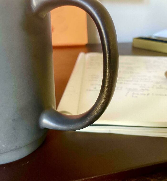 A mug handle resembling a letter "C" on a desk with notepads, capturing mildly interesting details.