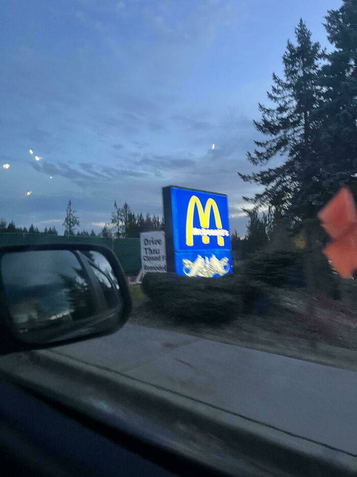 McDonald's drive-thru sign at dusk, viewed from a car, offering mildly interesting visual amid trees and cloudy sky.