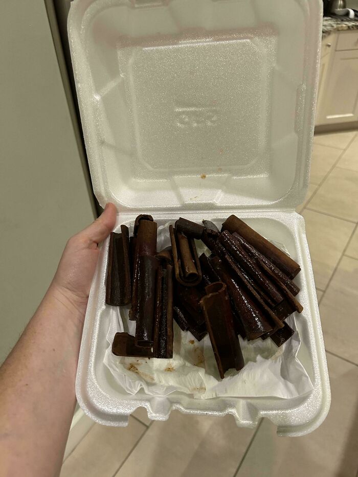 Hand holding a takeout container filled with mildly interesting cinnamon sticks.